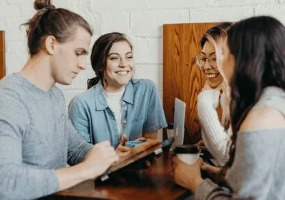 A group of people are together, chatting and smiling as they work together. Their friendly, dynamic atmosphere reflects effective collaboration.