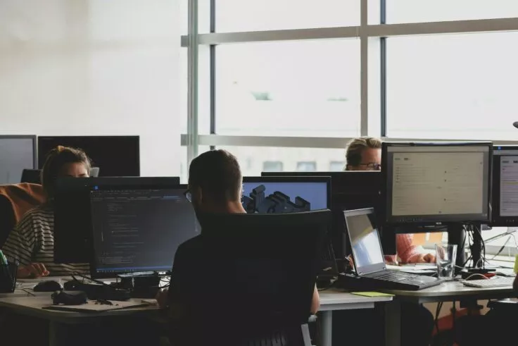 Several people work in an open space, each in front of his or her own computer.