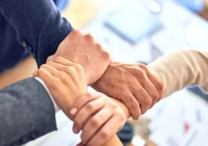 A set of hands from different people come together in the center of the image, symbolizing teamwork and collaboration.