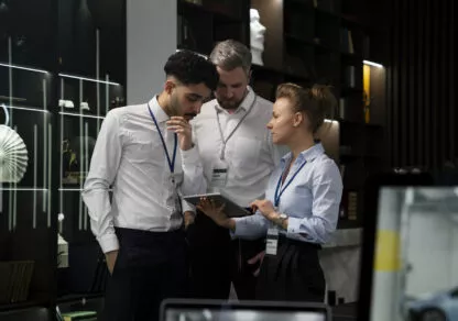 Three people are standing, discussing their work around a woman holding a tablet. The faces are attentive and engaged, illustrating a dynamic exchange of ideas.