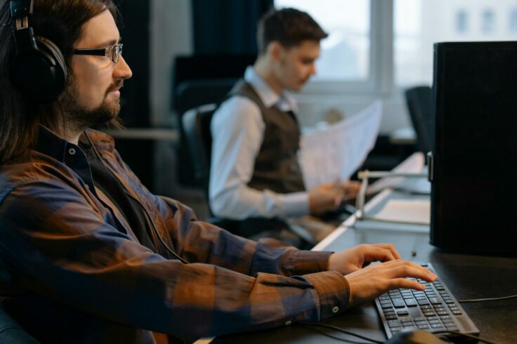 Two people sit in front of their computers, focused on screens that represent expert monitoring and assistance 24 hours a day, 7 days a week.