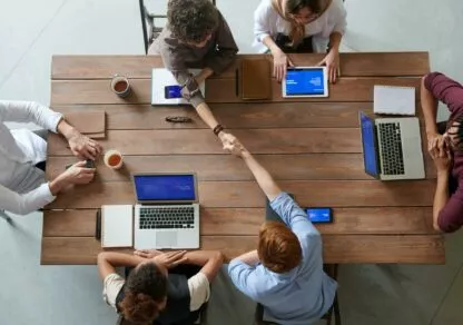 Plusieurs personnes en réunion dont 2 personnes qui se sert la main en signe de collaboration