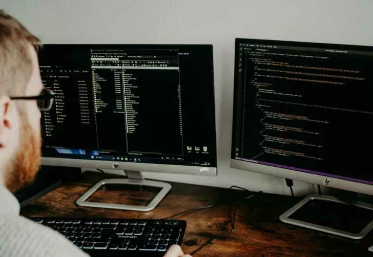 One person is sitting in front of two computer screens, concentrating on his work.